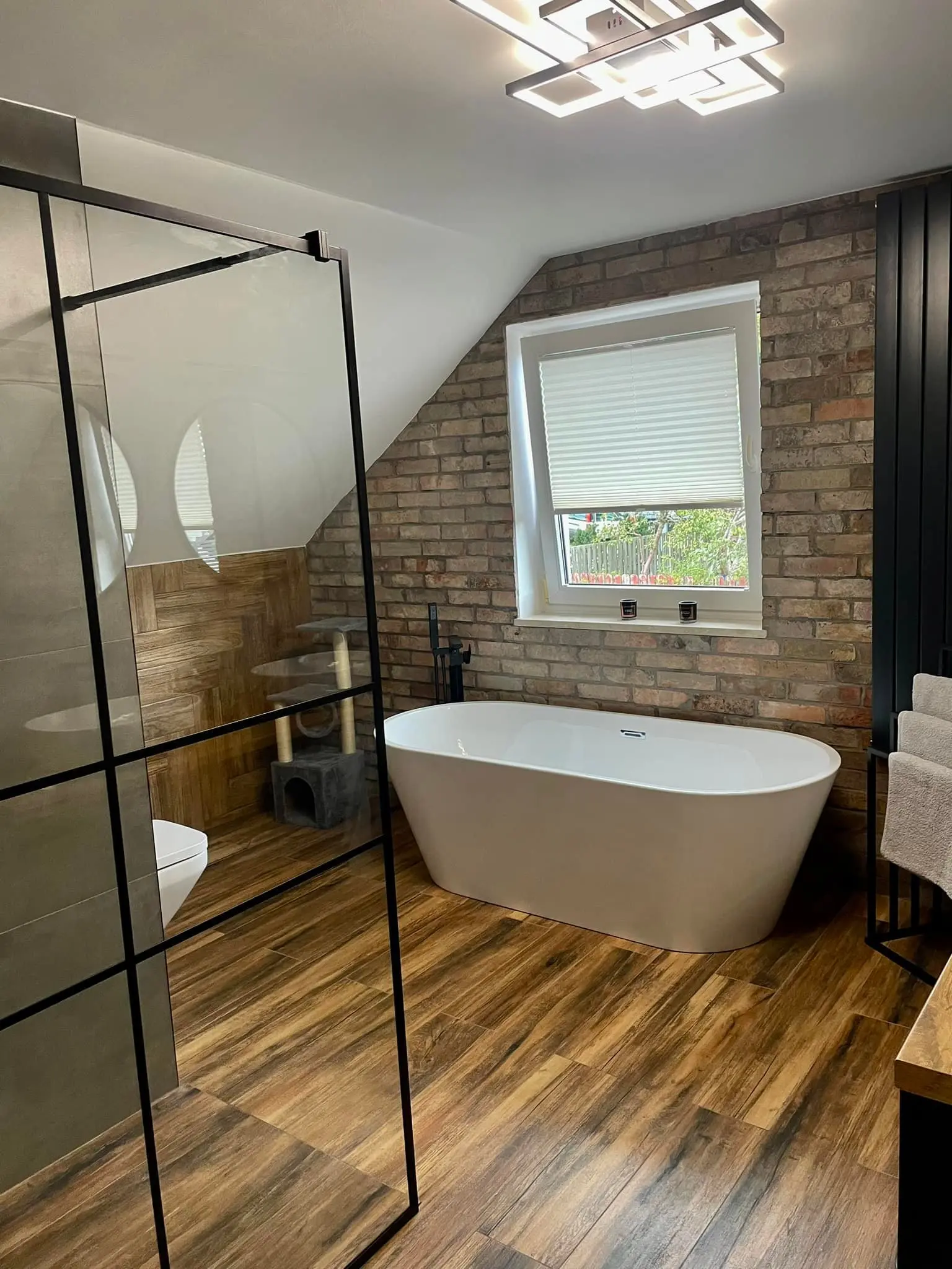 Luksusowy projekt łazienki na poddaszu, wanna wolnostojąca, ściana z czerwonej cegły i podłoga z gresu drewnopodobnego - REM-BUD